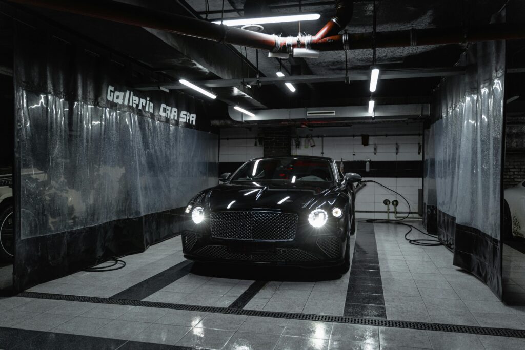 Sleek black car with headlights on, parked in a stylish garage with bright lighting.